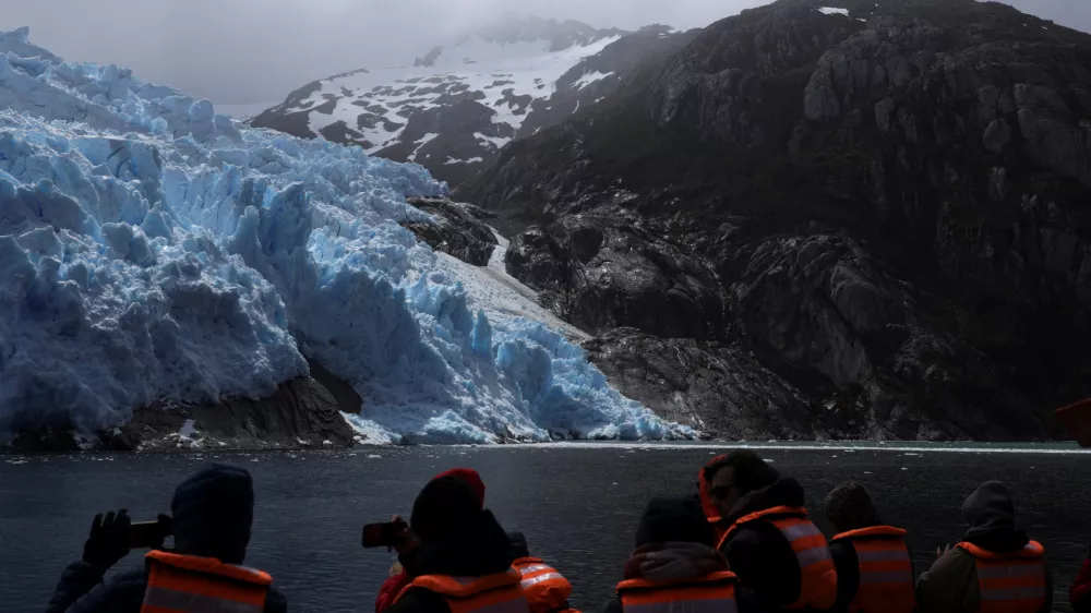 Tourists take photographs of the Sarmiento de Gamboa glacier in front of Santa Ines Island with their cell phones, during a boat trip in the Strait of Magellan, near the Brunswick Peninsula where Chile plans to create Cape Froward National Park to protect roughly 150,000 hectares of forests, peatlands, glaciers and coastline, in collaboration with Rewilding Chile, in Punta Arenas, Chile, December 2, 2025. REUTERS/Pablo Sanhueza