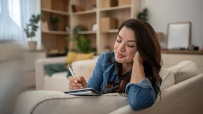 Young woman feeling happy and relaxed while writing personal notes in a diary or journal, reflecting on her day in the comfort of her cozy home environment / Foto: Mirjana Pusicic, Getty Images