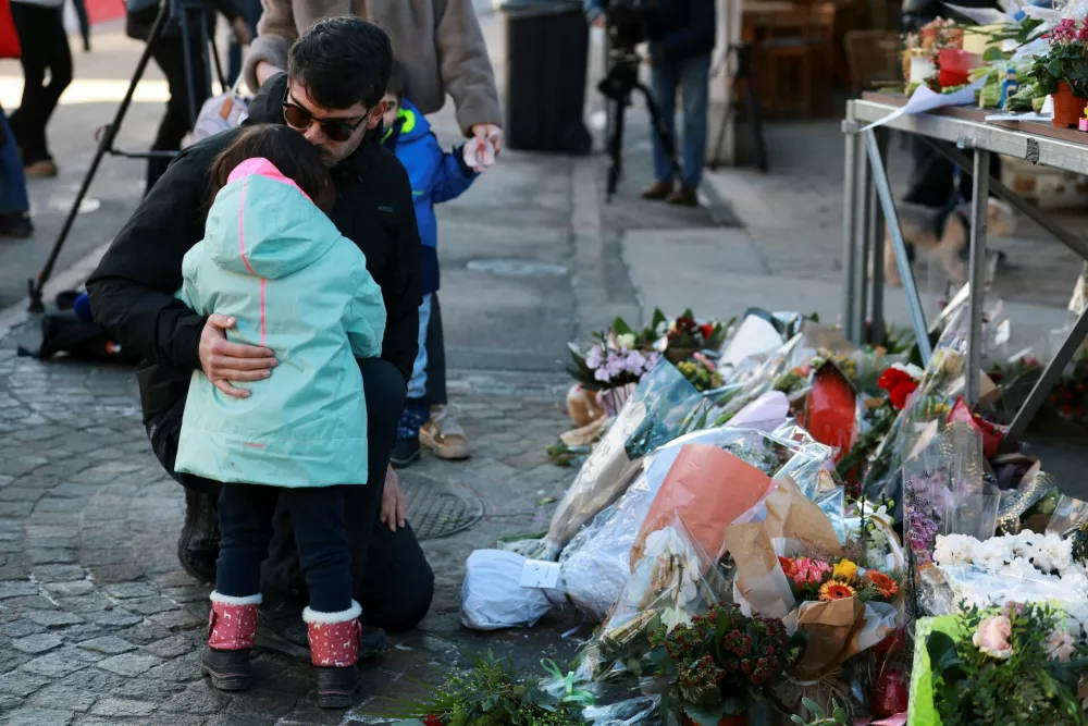 A man embraces a child next to the tributes laid for the victims outside the "Le Constellation" bar, after a fire and explosion during a New Year's Eve party where several people died and others were injured in the upscale ski resort of Crans-Montana in southwestern Switzerland, January 2, 2026. REUTERS/Stephanie Lecocq