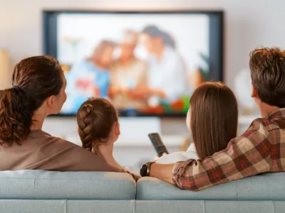 Happy family spending time together. Mother, father and children watching TV, movies with popcorn in the evening at home.
