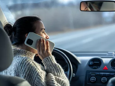 Young woman talking on the phone while driving a car, inside view.