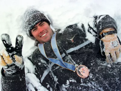 FILE - Swiss snowboarder Ueli Kestenholz rolls around in the snow of Shiga Kogen on Monday, Feb. 9, 1998, adorned with the bronze medal he won the previous day in the Olympic snowboard giant slalom. (Alessandro della Valle/Keystone via AP, file)