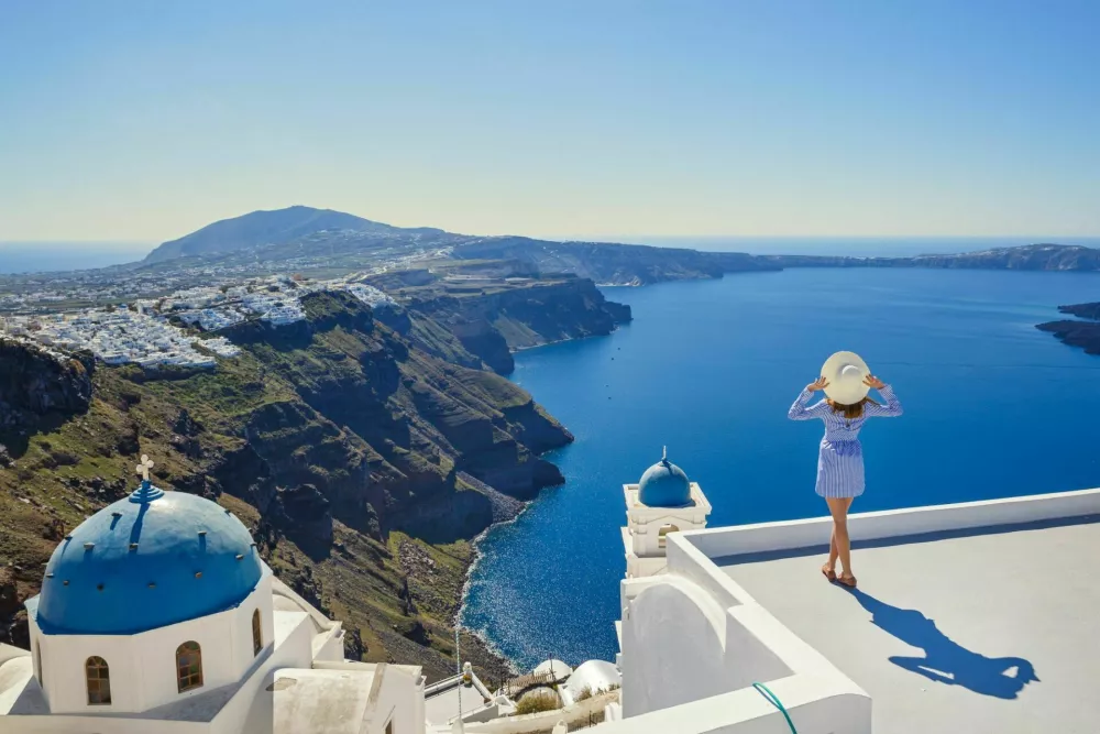 Young woman stands on a hill and looks at the marine landscape of Santorini, Greece / Foto: Santorines