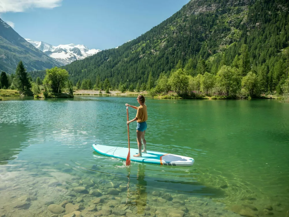Stand up paddle with a view, woman on SUP in the mountains looking at glacier forest and mountain range. Girl enjoying outdoor activities on alpine lake / Foto: Mystockimages
