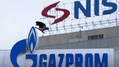 A raven flies between the NIS "Naftna industrija Srbije" (Petroleum Industry of Serbia) on an office building and the Gazprom company logo at a petrol station in Belgrade, Serbia, Sunday, Nov. 23, 2025. (AP Photo/Darko Vojinovic)