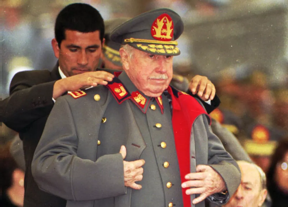 FILE - In this Aug. 23, 1995 file photo, former Chilean dictator and military commander Gen. Augusto Pinochet is helped by a bodyguard to put on his coat during a military ceremony in Santiago, Chile, on the occasion of the 22nd anniversary of his taking the post as head of the Chilean armed forces. Months after his appointment in 1973, Pinochet led the coup that ousted President Salvador Allende. Pinochet sympathizers will honor the former strongman on Sunday, June 10, 2012 with the screening of a new documentary about his dictatorship years in a Santiago theater. (AP Photo/Santiago Llanquin, File)