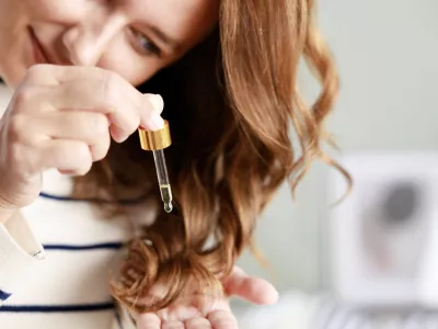 Young woman cares for her hair with cosmetic oil. Cosmetic oil for hair in a pipette. Liquid drop dripping on wavy brown hair