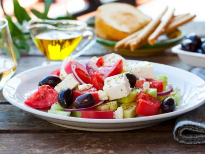 Greek salad. Fresh vegetables, feta cheese and black olives with white wine. Outdoor background.