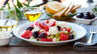 Greek salad. Fresh vegetables, feta cheese and black olives with white wine. Outdoor background.