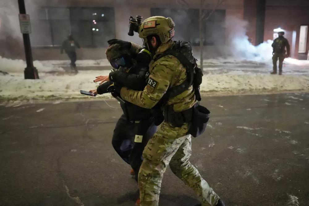 A federal agent holds a person as the agents try to clear the demonstrators near a hotel, using tear gas during a noise demonstration protest in response to federal immigration enforcement operations in the city Sunday, Jan. 25, 2026, in Minneapolis. (AP Photo/Adam Gray)