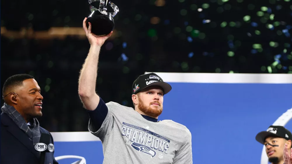 Jan 25, 2026; Seattle, WA, USA; Seattle Seahawks quarterback Sam Darnold (14) celebrates with the trophy on the podium after defeating the Los Angeles Rams in the 2026 NFC Championship Game at Lumen Field. Mandatory Credit: Kevin Ng-Imagn Images