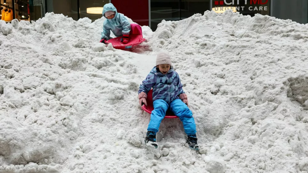 Children sled and play on a snow pile outside the New York Stock Exchange (NYSE), after a major winter storm spreads across a large swath of the United States, in New York City, U.S., January 26, 2026. REUTERS/Brendan McDermid / Foto: Brendan Mcdermid