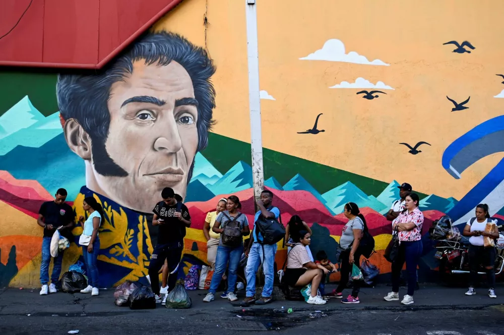 People wait for public transportation beside a wall painted with an image of Simon Bolivar, in Caracas, Venezuela, January 31, 2026. REUTERS/Maxwell Briceno