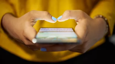 Young woman using cell phone to send text message on social network at night. Closeup of hands with computer laptop in background
