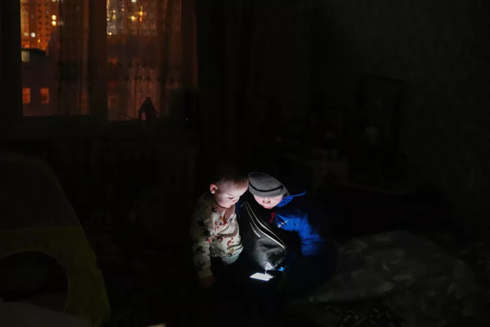 Daniil Dolotov, 11, plays on a phone with his brother Bohdanchyk, 18 months, in their apartment during a power outage caused by Russia's repeated air strikes on the country's power grid, in Kyiv, Ukraine, Monday, Feb. 2, 2026. (AP Photo/Sergey Grits)