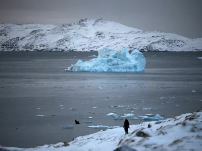 A person walks on the shore as a small iceberg floats in the sea near Nuuk, Greenland, February 4, 2026. REUTERS/Stoyan Nenov