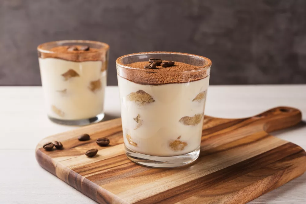 Homemade Italian tiramisu dessert with cocoa powder in glasses on light wooden table. / Foto: Galina Oleksenko