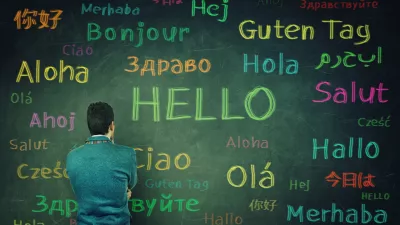 Rear view of a puzzled businessman in front of a huge chalkboard written with the word hallo in different languages and colors. Opportunity for learning many languages for students. / Foto: Bulat Silvia