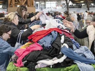 France, 2025-04-04. Emmaus flea market in Poitiers. Sitting on either side of a large table strewn with second-hand clothes, people frantically search for those that might suit them. The hyper-consumerism of the French means that twice a year, the Emmaus companions organise a big jumble sale to get rid of their stocks of unsold goods. You ll find mountains of second-hand clothes, books, furniture and crockery at low prices. Photograph by Jean-Francois Fort / Hans Lucas.France, 2025-04-04. Braderie Emmaus a Poitiers. Installees part et d autres d une grande table jonchee de vetements d occasions, des personnes recherchent avec attention ceux qui pourraient leur convenir. L hyper consommation des Francais fait que 2 fois par ans les compagnons d Emmaus organisent une grande braderie pour se debarrasser de leurs stocks d invendus. On y trouve de veritables montagnes de vetements, de livres, de meubles, de vaisselle, d occasion et a petit prix. Photographie de Jean-Francois Fort / Hans Lucas.