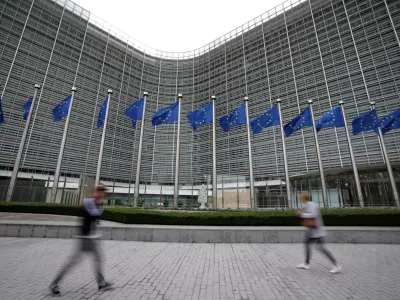 FILE - European Union flags wave in the wind as pedestrians walk by EU headquarters in Brussels, on Sept. 20, 2023. The European Union's powerful Commission announced on Thursday that it will start releasing billions of euros to Poland after the funds were frozen over the previous government's policies that the bloc said amounted to widespread backsliding of fundamental democratic principles. (AP Photo/Virginia Mayo, File)