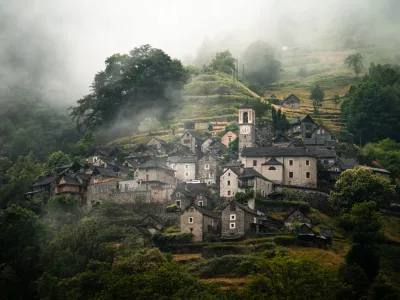 A foggy morning view of Corippo village nestled in the lush green hills with a prominent church tower in Lavertezzo, switzerland
