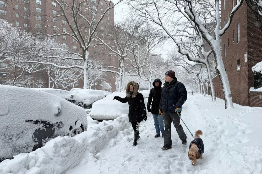 People walk with a dog alongside snow laden parked cars in a snowstorm, Monday, Feb. 23, 2026, in New York. (AP Photo/Pamela Hassell)