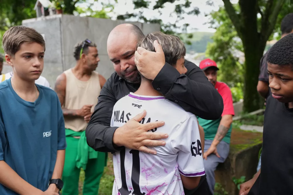Ricardo Dutra, the father of 11-year-old Bernardo Lopes, a victim of heavy rains and flooding, is comforted by his son's friends during the funeral and burial of his child in Juiz de Fora, Minas Gerais state, Brazil Wednesday, Feb. 25, 2026. (AP Photo/Silvia Izquierdo)