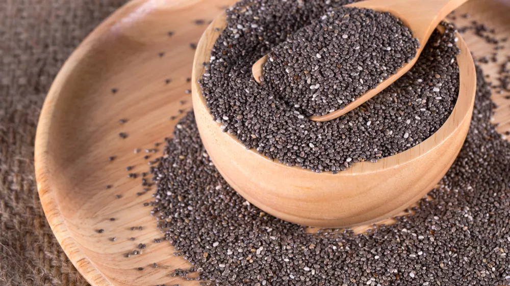 chia seeds in wooden bowl on wooden plate and wooden spoon of chia seeds on top. selective focus. on burlap background.