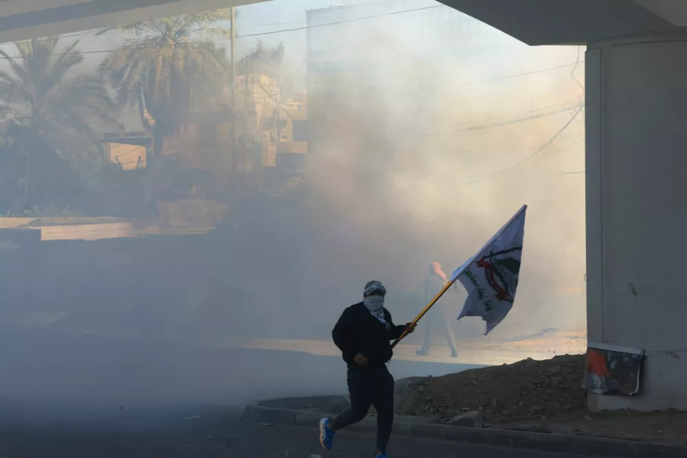 A person holds a flag after riot police deployed irritants to disperse protesters supporting Iraqi Shi'ite armed groups gathered near the entrance of the Green Zone and attempted to move toward the U.S. embassy after the killing of Iran's Supreme Leader Ayatollah Ali Khamenei, in Baghdad, Iraq, March 1, 2026. REUTERS/Thaier Al-Sudani