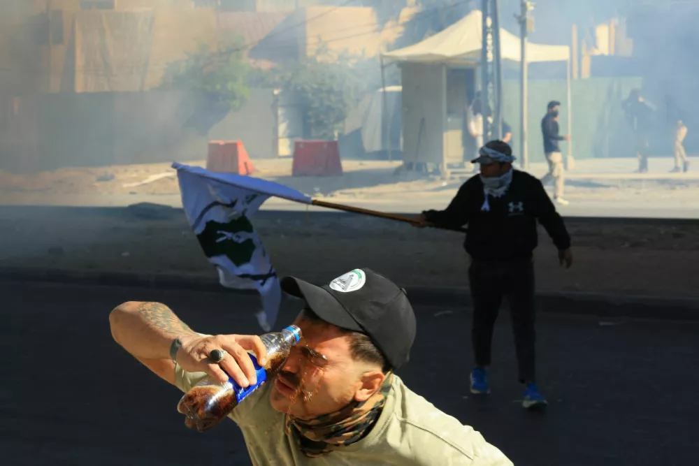 A person washes his face with a soft drink bottle after riot police deployed irritants to disperse protesters supporting Iraqi Shi'ite armed groups gathered near the entrance of the Green Zone and attempted to move toward the U.S. embassy after the killing of Iran's Supreme Leader Ayatollah Ali Khamenei, in Baghdad, Iraq, March 1, 2026. REUTERS/Thaier Al-Sudani   TPX IMAGES OF THE DAY