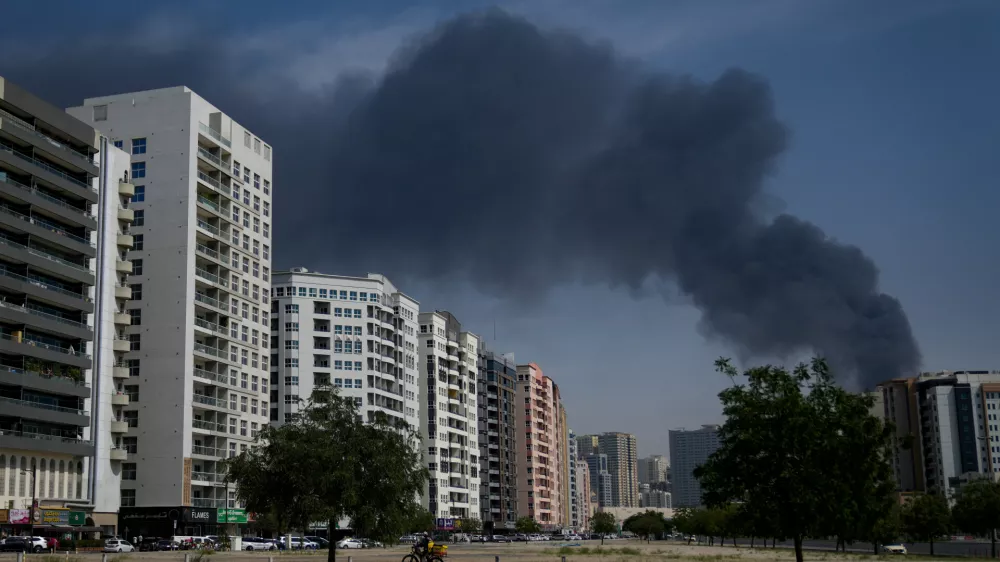 A cyclist rides past as black plume of smoke is seen rising from a warehouse at the industrial area of Sharjah City in the United Arab Emirates following reports of Iranian strikes in Dubai, United Arab Emirates, Sunday, March 1, 2026. (AP Photo/Altaf Qadri)