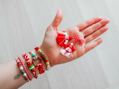 Bulgarian traditional spring decor martenitsa bracelets, holding in hand, wooden background. Baba Marta holiday, backdrop.