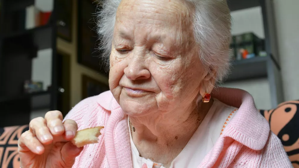 Old woman eating a slice of bread at home