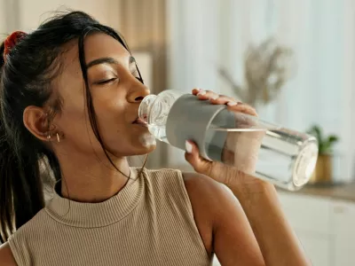 Drinking water, yoga or Indian woman in home with health, fitness or wellness for natural hydration. Thirsty female person, tired or healthy girl with liquid bottle after pilates to detox or relax