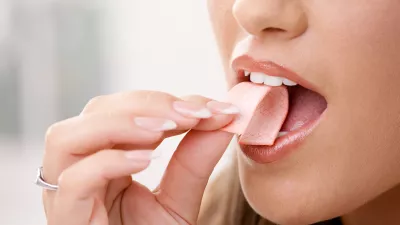 Closeup detail of woman putting pink chewing gum into her mouth.