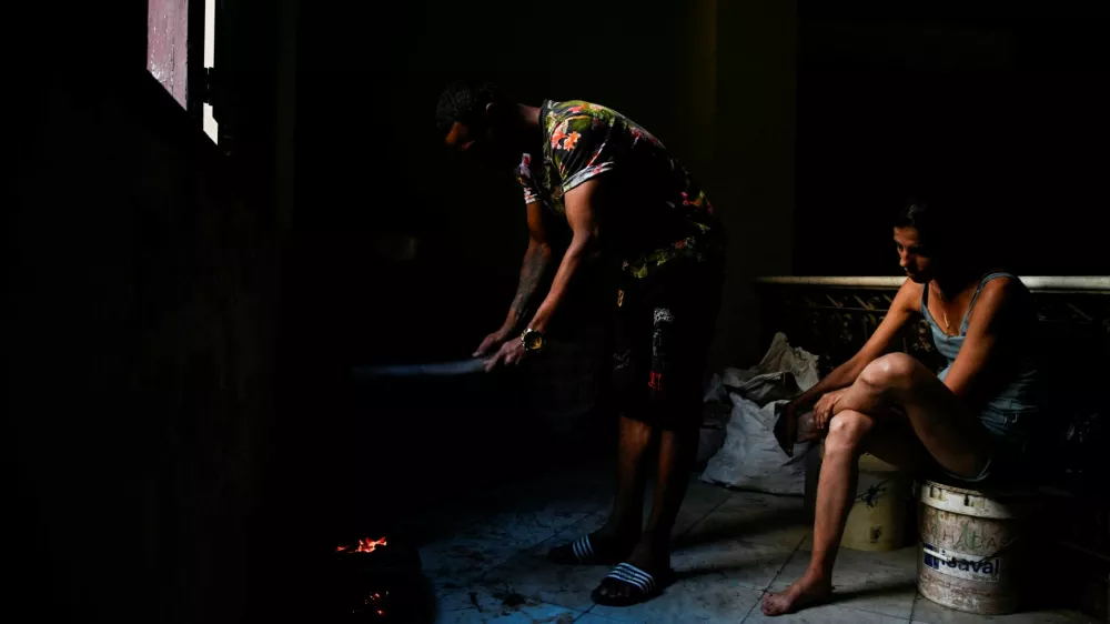 Jesus Rodriguez lights charcoal for cooking while his wife, Yaliet Iglesias, sits nearby as Cuba's national electric grid collapsed for the second time in a week amid the U.S.-imposed oil blockade, according to officials, as the communist government struggles to keep the lights on for about 10 million people with decrepit infrastructure, in Havana, Cuba, March 21, 2026. REUTERS/Norlys Perez