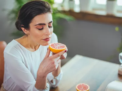 Sick woman trying to sense smell of half fresh orange, has symptoms of Covid-19, corona virus infection - loss of smell and taste. One of the main signs of the disease.