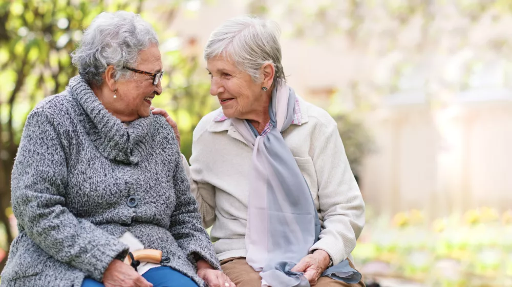Two elderly women sitting on bench in park smiling happy life long friends enjoying retirement