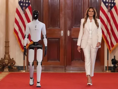 First lady Melania Trump arrives, accompanied by a robot, to attend the "Fostering the Future Together Global Coalition Summit," with other first spouses, at the White House, Wednesday, March 25, 2026, in Washington. (AP Photo/Jacquelyn Martin)