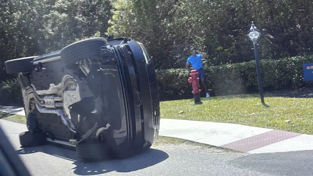 Golfer Tiger Woods stands by his overturned vehicle in Jupiter Island, Fla., on Friday, March 27, 2026. (AP Photo/Jason Oteri)