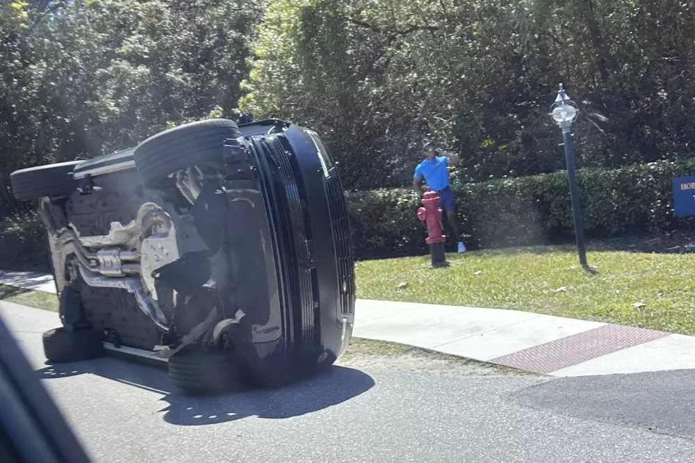 FILE- Golfer Tiger Woods stands by his overturned vehicle in Jupiter Island, Fla., March 27, 2026. (AP Photo/Jason Oteri, File)