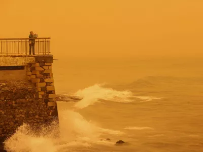 A woman takes pictures of the horizon turned yellow, caused by sand dust from the Sahara, due to strong southern winds, in Heraklion, Crete island, Greece April 1, 2026. REUTERS/Stefanos Rapanis