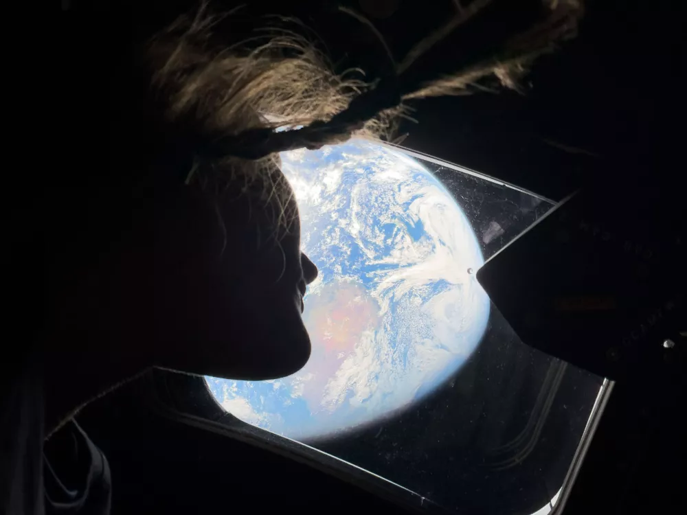 This image provided by NASA, astronaut and Artemis II mission specialist Christina Koch peers out of one of the Orion spacecraft's main cabin windows, looking back at Earth, as the crew travels towards the Moon on Thursday, April 2, 2026. (NASA via AP) / Foto: 