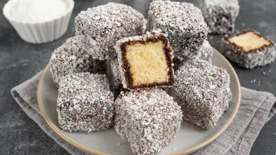 Traditional Australian Lamington cake in chocolate glaze and coconut flakes on a plate on a gray concrete background with a cup of tea. Selective focus / Foto: Irina Taskova