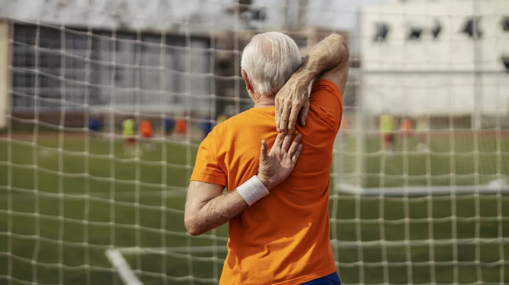 Rear view of senior sportsman standing on stadium and stretching his arms.