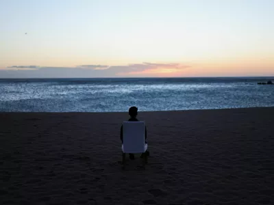 A tourist sits on a chair and looks out at sunrise on a beach in Barcelona, Spain, February 12, 2026. REUTERS/Nacho Doce / Foto: Nacho Doce