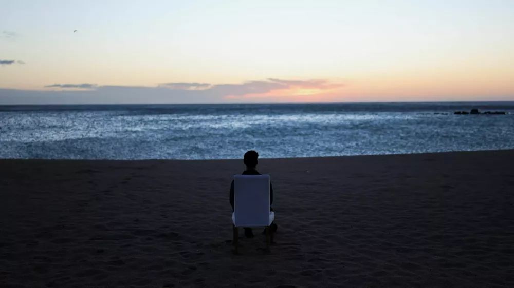 A tourist sits on a chair and looks out at sunrise on a beach in Barcelona, Spain, February 12, 2026. REUTERS/Nacho Doce / Foto: Nacho Doce