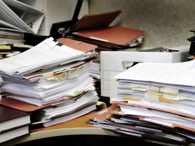 Detail of a messy desk with books binders files and papers stacked up high in a disorganized mess