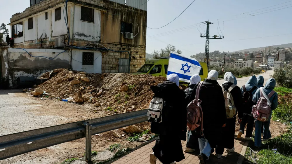People walk past a newly installed dirt barrier by the Israeli military at the main entrance to Luban e-Sharkiya, between Nablus and Ramallah, in the Israeli-occupied West Bank, February 16, 2026. REUTERS/Ammar Awad