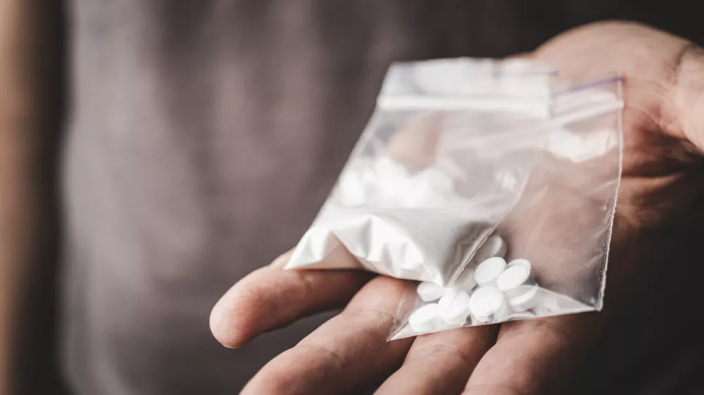 Man's hand holds two transparent plastic packets with cocaine powder and white pills lsd, drug dealer selling drugs. Drug abuse and addiction concept.